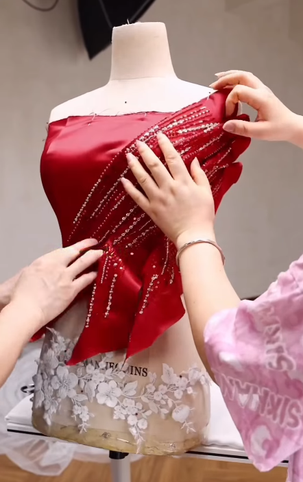 Tailor shaping folded beaded shoulder pleats on a red satin formal dress