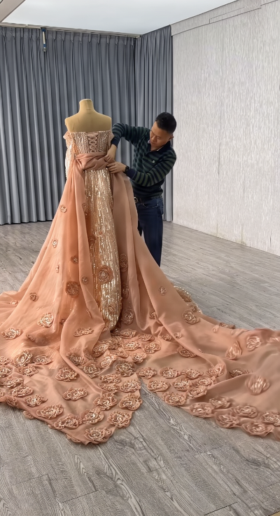 Tailor adjusting the luxurious floral-embellished detachable train on a mannequin to ensure the perfect drape and fall