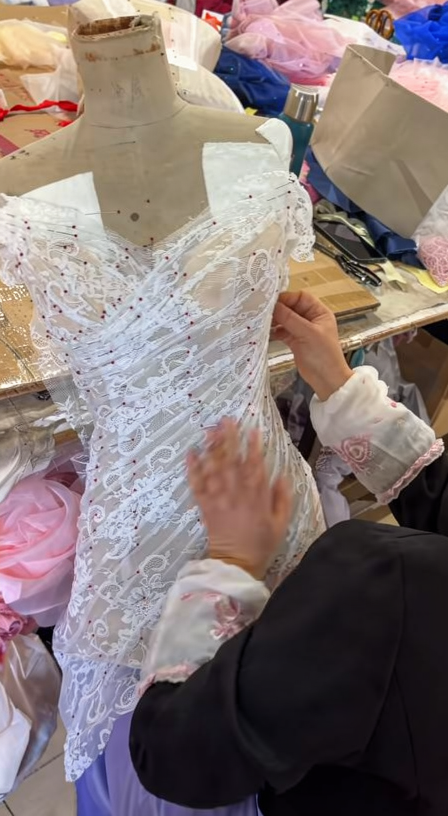 Tailor fixing layered eyelash lace folds on an ivory mermaid wedding dress mannequin
