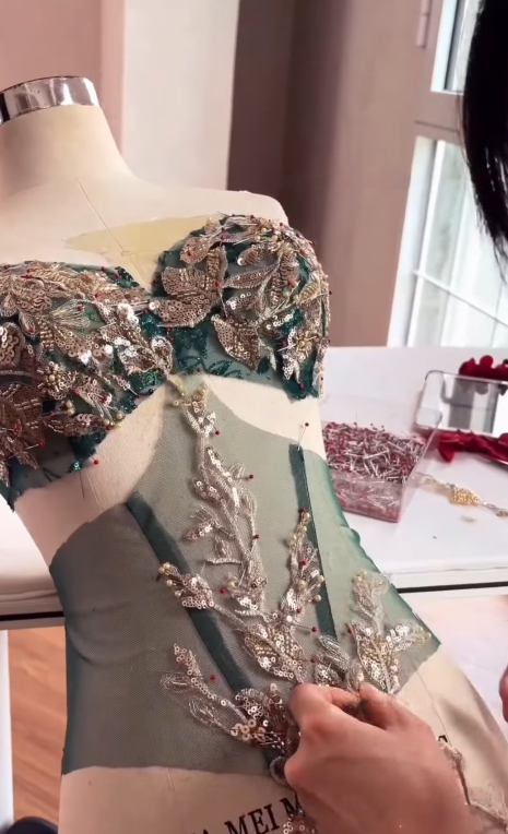 Tailor pinning decorative elements on green bodice