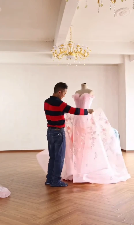 Tailors adjusting flowing tulle layers on a pink evening ball gown
