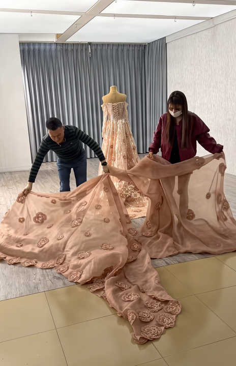 Two tailors carefully arranging the hundreds of hand-made flowers across the voluminous detachable train of the champagne pink gown