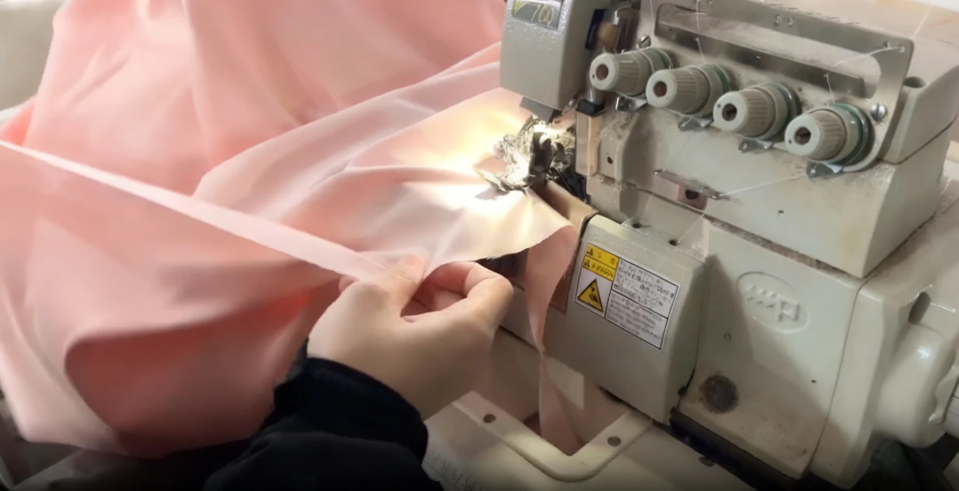 Dressmaker sewing pink tulle fabric with an industrial overlock machine during couture gown production