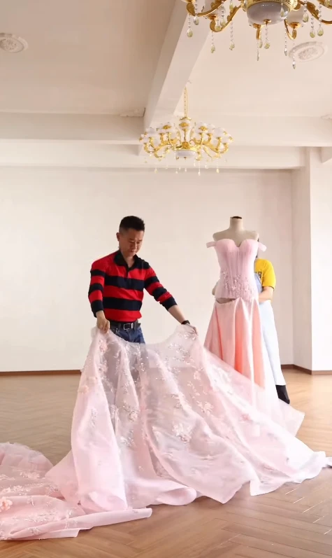 Workshop workers laying out long train material for a pink couture ball gown