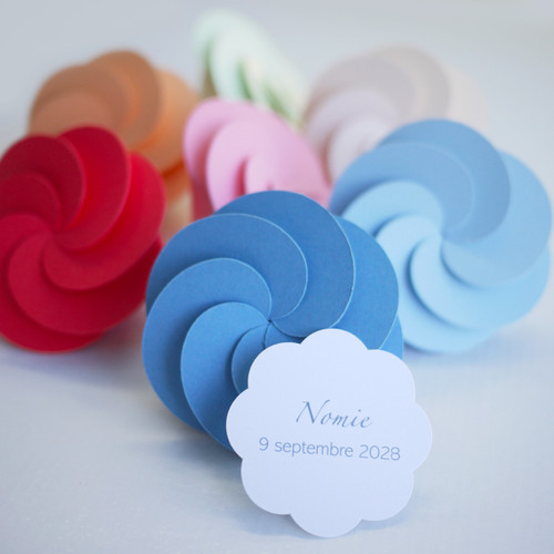 Boîte à dragées en forme de fleur, pliage savant et très marquant, peut accueillir 20 g de dragées et une étiquette personnalisée au prénom de votre enfant, imprimée à l'encre noire ou de la couleur de la boîte