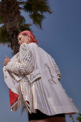 Kashesh Maham Coat in Ivory: A cream and gold handwoven mid-length women's jacket featuring dramatic shoulders and gold sequin embroidery reading 'Impossible' and 'Dream,' revealed against a luxurious red silk lining