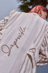 Kashesh Maham Coat in Ivory: A cream and gold handwoven mid-length women's jacket featuring dramatic shoulders and gold sequin embroidery reading 'Impossible' and 'Dream,' revealed against a luxurious red silk lining