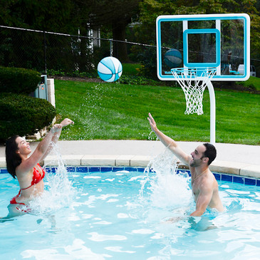 Man and woman playing poolside basketball with Deck Shoot hoop and Splash-It ball in backyard swimming pool