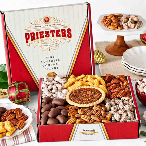 Priester’s red and gold gift box filled with assorted pecans, milk chocolatey pecans, cheese straws, and a mini pecan pie, displayed with Christmas ornaments.
