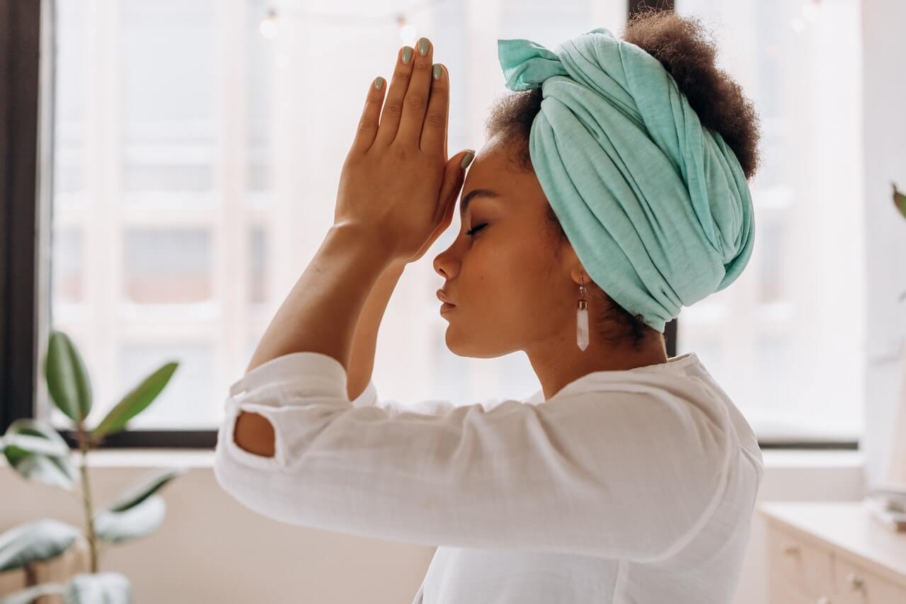 Woman wearing blue headscarf with eyes closed and her palms together