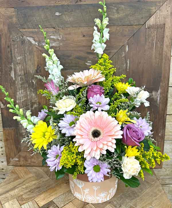 Spring flower arrangement with peach gerbera daisy lavender roses yellow daisies and pastel blooms in decorative container
