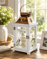 White memorial keepsake lantern with a stainless steel copper finish top and inspirational sentiment, displayed on a table in a peaceful home setting with natural sunlight and soft floral accents.