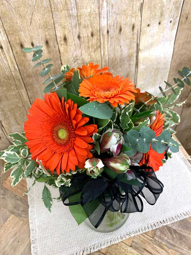 Gerbera daisy with color  accent flowers and specialty greens and bow