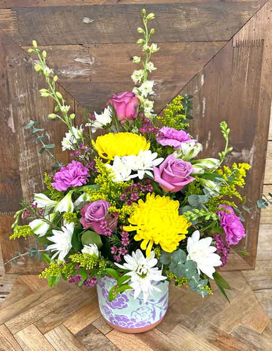 Bright spring flower arrangement with yellow mums lavender roses and daisies in decorative vase