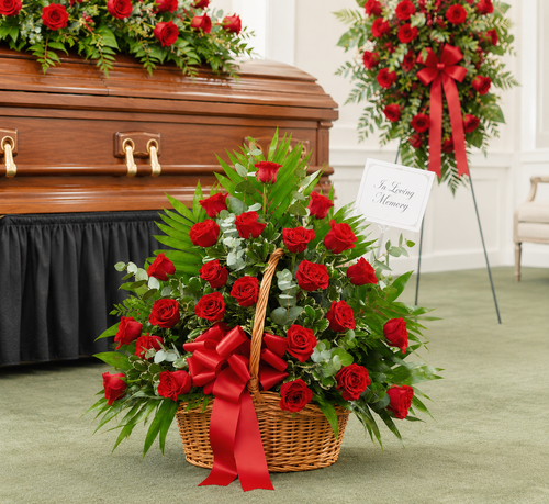 Elegant funeral roses arranged in a wicker basket displayed beside a casket at a memorial service.