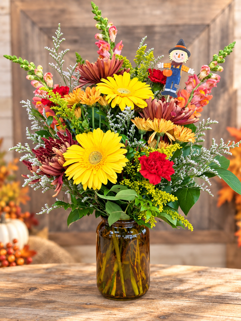 Scarecrow Sunshine fall flower arrangement with yellow gerbera daisies, autumn mums and scarecrow accent in an amber vase