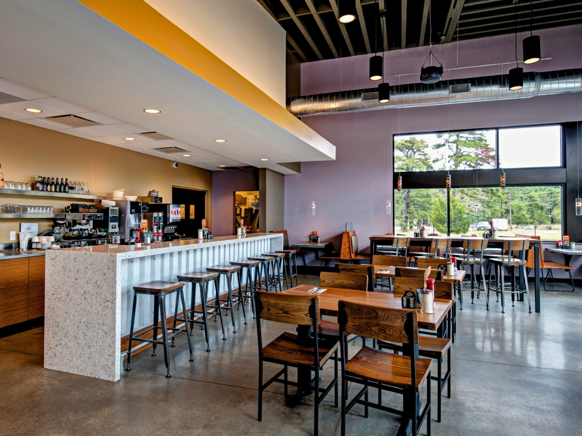 Modern restaurant interior with wood and metal dining chairs, bar stools, and communal seating