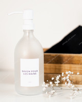 Flacon distributeur en verre givré à pompe blanche, étiquette Savon pour les mains, devant une cagette en bois et un brin de gypsophile