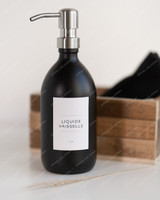 Flacon distributeur en verre noir mat à pompe inox, étiquette Liquide vaisselle, devant une cagette en bois et un linge noir