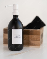 Flacon distributeur en verre noir à pompe blanche, étiquette Liquide vaisselle, devant une cagette en bois et un linge noir