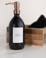 Flacon distributeur en verre noir mat à pompe cuivre, étiquette Liquide vaisselle, devant une cagette en bois et un linge noir