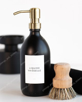 Flacon distributeur en verre noir à pompe dorée, étiquette Liquide vaisselle, à côté d'une brosse à vaisselle en bois et d'un pot noir
