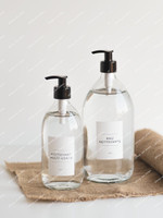 Deux distributeurs de savon en verre transparent à pompes noires, étiquettes Nettoyant multi usage et Eau nettoyante, sur une toile de jute