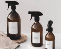 Spray nettoyant maison en verre ambré, trois tailles à gâchette noire, posées près d'un linge beige