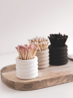 Trois pots à allumettes en céramique cannelée sur une planche en bois, garnis d'allumettes à têtes roses, blanches et de tiges entièrement noires