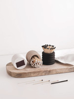 Trois pots à allumettes en céramique cannelée sur une planche en bois, deux couchés laissant voir le grattoir marron, allumettes éparses devant