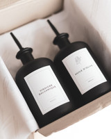 Vue plongeante dans le coffret ouvert : deux bouteilles noires mates à bec verseur, étiquettes Vinaigre balsamique et Huile d'olive, papier de soie