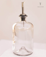 Bouteille en verre transparent équipée d'un bec verseur entièrement argenté, sur un linge blanc et fond beige