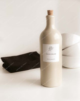 Bouteille huilier en grès beige fermée par un bouchon en liège, étiquette Huile d'olive, à côté d'un torchon noir et de bols blancs