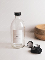 Bouteille en verre transparent étiquetée Javel, fermée par un bouchon noir, avec trois autres bouchons noirs posés à côté