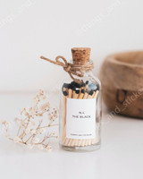 Flacon d'allumettes en verre à bouchon liège et ficelle, étiquette N.4 The Black, têtes noires, près d'un brin de gypsophile et d'un panier en bois