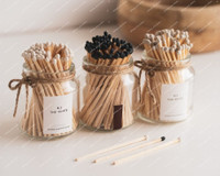 Trois pots à allumettes en verre noués de ficelle : N.2 The White, un pot d'allumettes noires avec grattoir, et N.5 The Beige