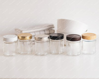 Six pots à épices en verre alignés, un par couleur de couvercle : blanc, doré, argenté, noir, marron chocolat et bois clair
