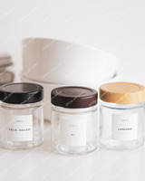 Trois pots à épices ronds en verre à couvercles noir, marron et bois, étiquettes Epices Ras el hanout, Ail et Curcuma
