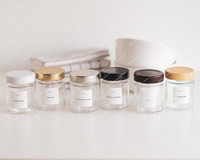 Six pots à épices ronds alignés, couvercles blanc, doré, argent, noir, marron et bois, étiquettes Gingembre, Paprika, Poivre blanc et autres