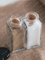 Gros plan de deux pots à épices carrés en verre, poivre et sel, chacun avec une petite cuillère en bois plantée dedans