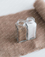Deux pots à épices carrés en verre ouverts, remplis de poivre et de sel, posés sur une toile de jute enroulée