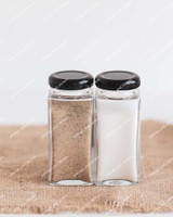 Deux pots à épices carrés en verre à couvercles noirs, remplis de poivre et de sel, posés sur une toile de jute