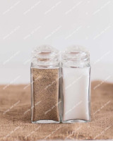 Deux pots à épices carrés en verre à couvercles saupoudreurs transparents, remplis de poivre et de sel, sur une toile de jute