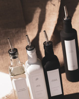Vue plongeante de quatre huiliers carrés à becs verseurs argentés pour huile et vinaigre, ombres portées sur une toile de jute
