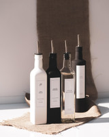 Quatre huiliers carrés à becs verseurs argentés pour huile et vinaigre, blanc, noir, transparent et noir, sur un carré de jute