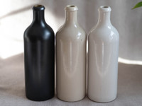 Trois huiliers en grès sans bec verseur, noir, beige et blanc cassé, sur une nappe de lin