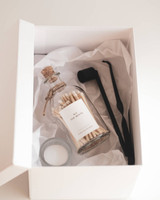 Coffret d'allumettes personnalisées ouvert, flacon à têtes blanches, bougie et accessoires noirs sur papier de soie