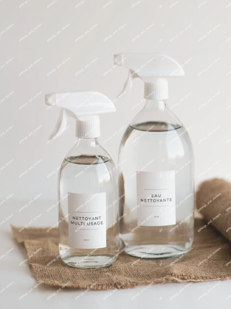 Deux bouteilles pulvérisateur en verre transparent à gâchettes blanches, étiquettes Nettoyant multi usage et Eau nettoyante, sur une toile de jute