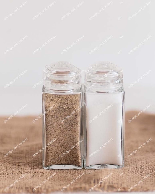 Deux pots à épices carrés en verre à couvercles saupoudreurs transparents, remplis de poivre et de sel, sur une toile de jute