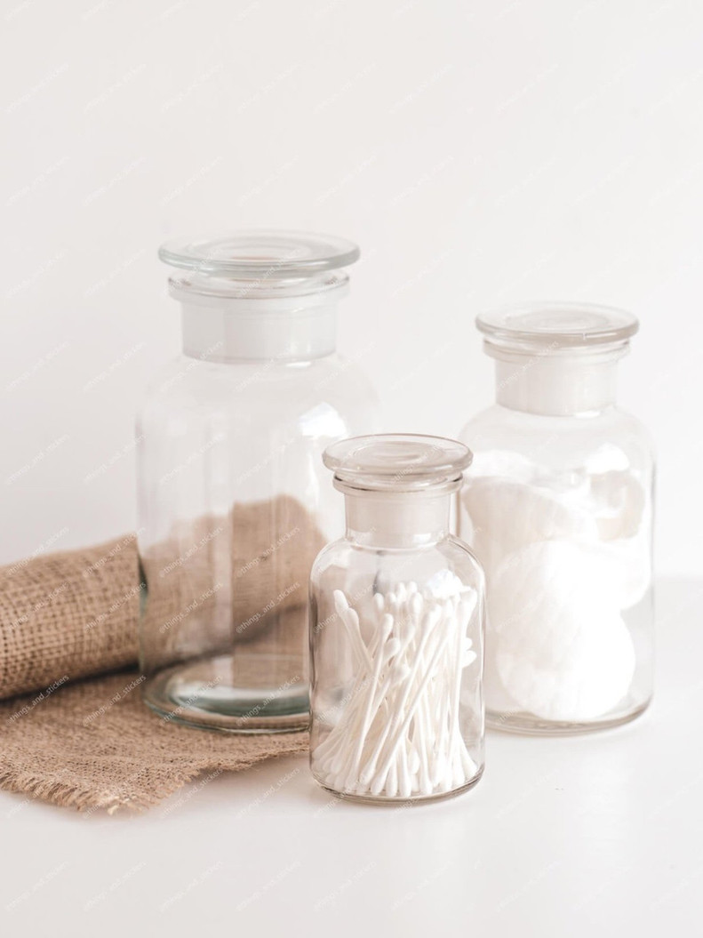 Trois bocaux apothicaire en verre transparent à couvercle, remplis de cotons-tiges et de cotons, posés près d'une toile de jute